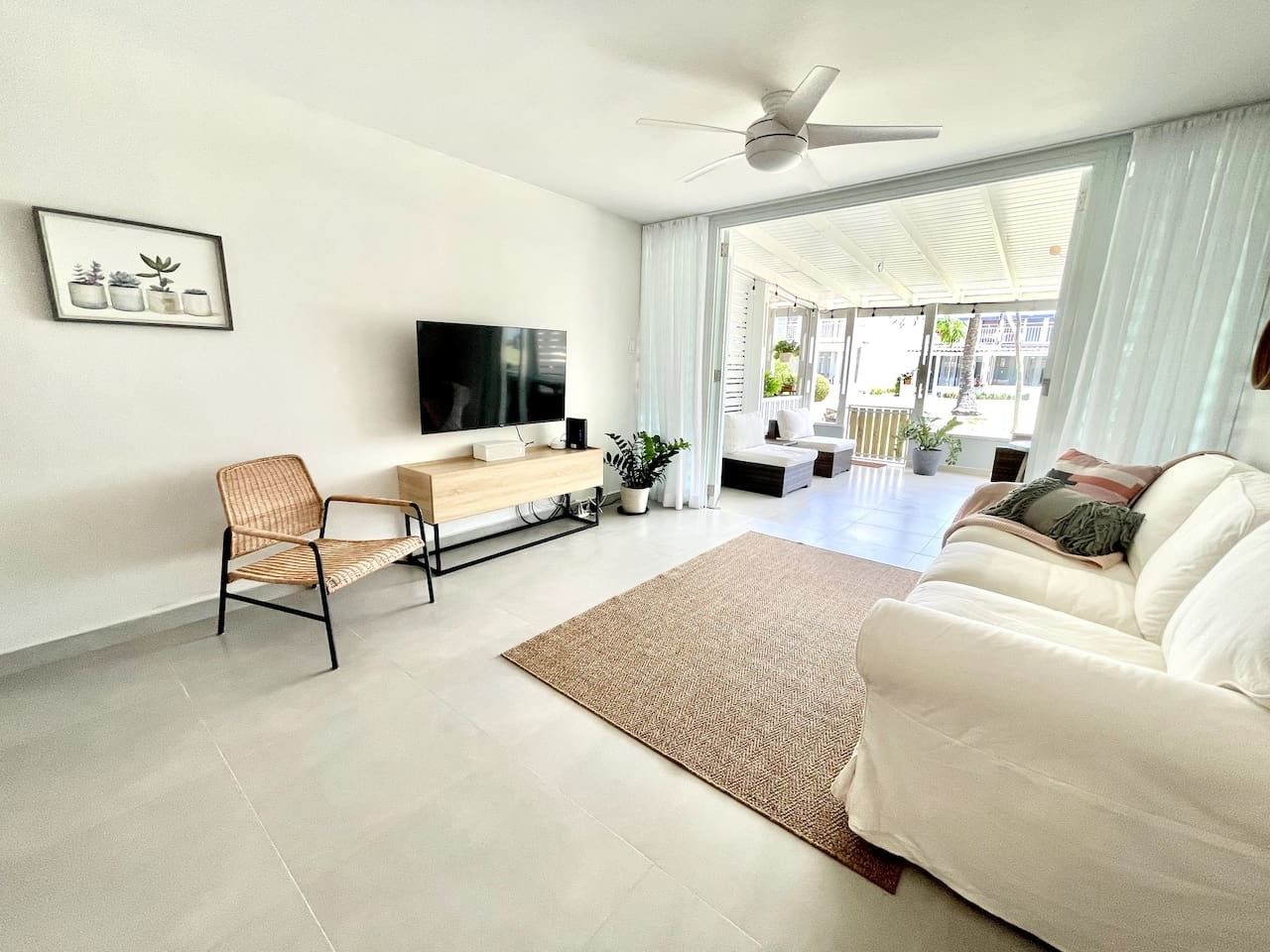 Una sala de estar moderna con un sofá, una silla, un televisor, un ventilador de techo y vistas al exterior.