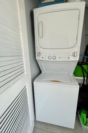 A compact laundry room with a washing machine and dryer stacked vertically. - CoCo Beachfront self check-in, pool and parking (Dorado)