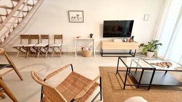A modern living room with a TV, wicker chairs, a glass coffee table, and a staircase.