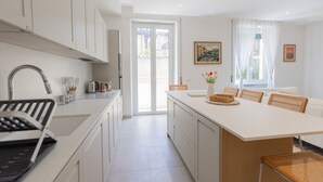 A modern kitchen with white cabinetry, a central island, and a dining area with wicker chairs. - GuestHost - Bright Apartment near Vatican City (Rome)