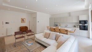 A modern living room with a sofa, chairs, a dining table, and a kitchen area with cabinets and appliances. - GuestHost - Bright Apartment near Vatican City (Rome)