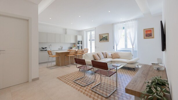A modern living room with a sofa, coffee table, and chairs, a kitchen area with white cabinets, and a dining space with a table and chairs. - GuestHost - Bright Apartment near Vatican City (Rome)
