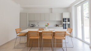 A modern kitchen with white cabinets, a central island with chairs, and a large window. - GuestHost - Bright Apartment near Vatican City (Rome)