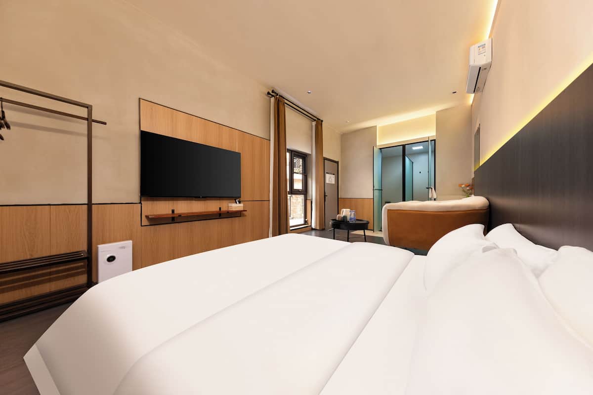 A hotel room with a large bed, a flat-screen TV mounted on the wall, a small table with a chair, and a bathroom door.