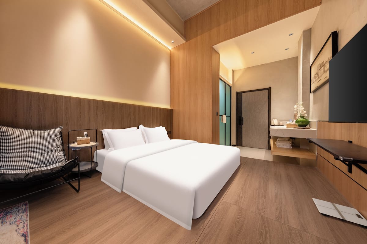 A modern hotel room with a large bed, a small seating area, a vanity with a mirror, and a wooden floor.