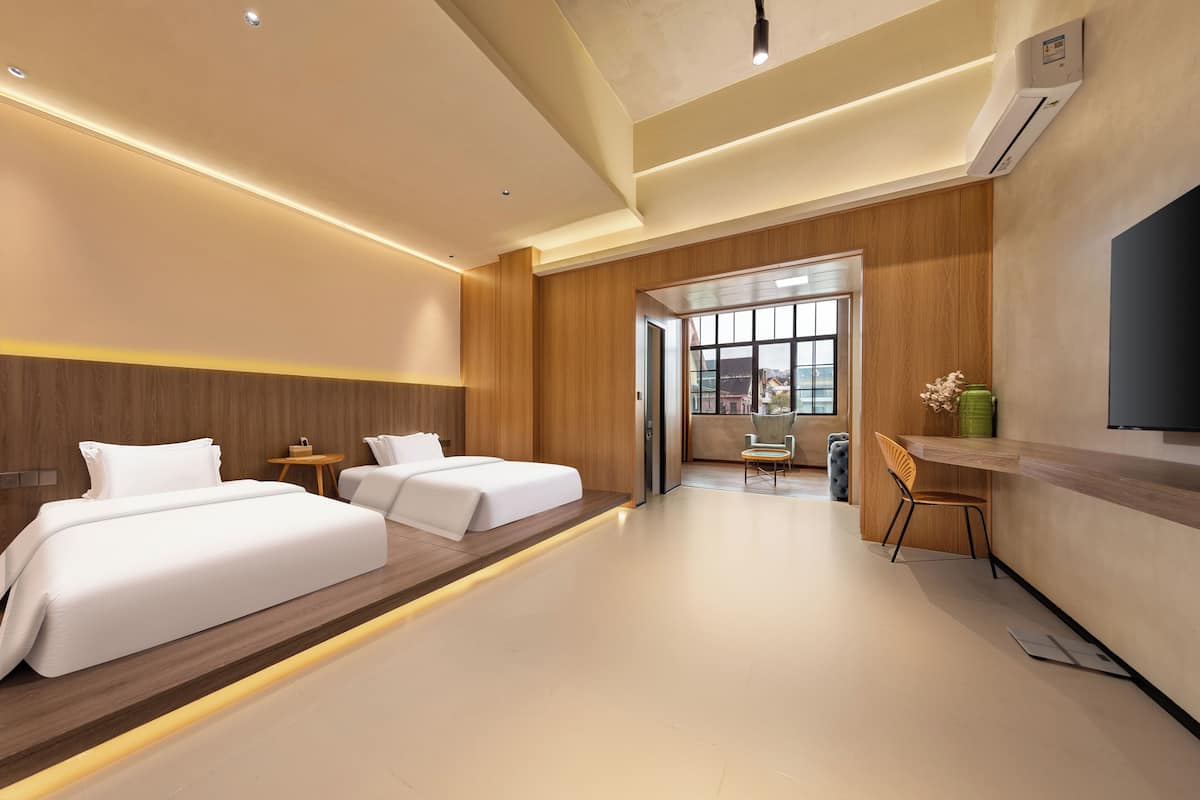 A hotel room with two beds, a desk, a chair, and a large window.