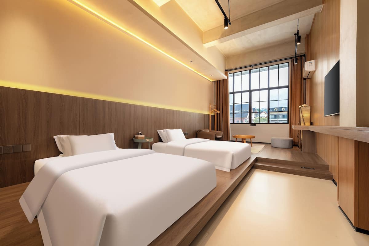 A modern hotel room with two beds, a wooden accent wall, a large window, and a flat-screen TV.