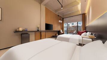 A modern hotel room with a flat-screen TV, a sofa, a small table, and a view of the outside.