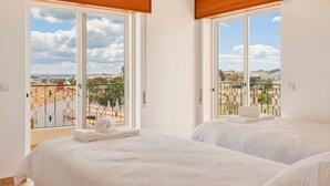Een hotelkamer met twee bedden, grote ramen en een balkon met uitzicht op de stad.