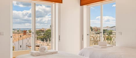 A hotel room with two beds, large windows, and a balcony with a view of the city.