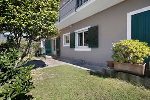 Un edificio residencial con entrada pavimentada, contraventanas verdes y un pequeño jardín.
