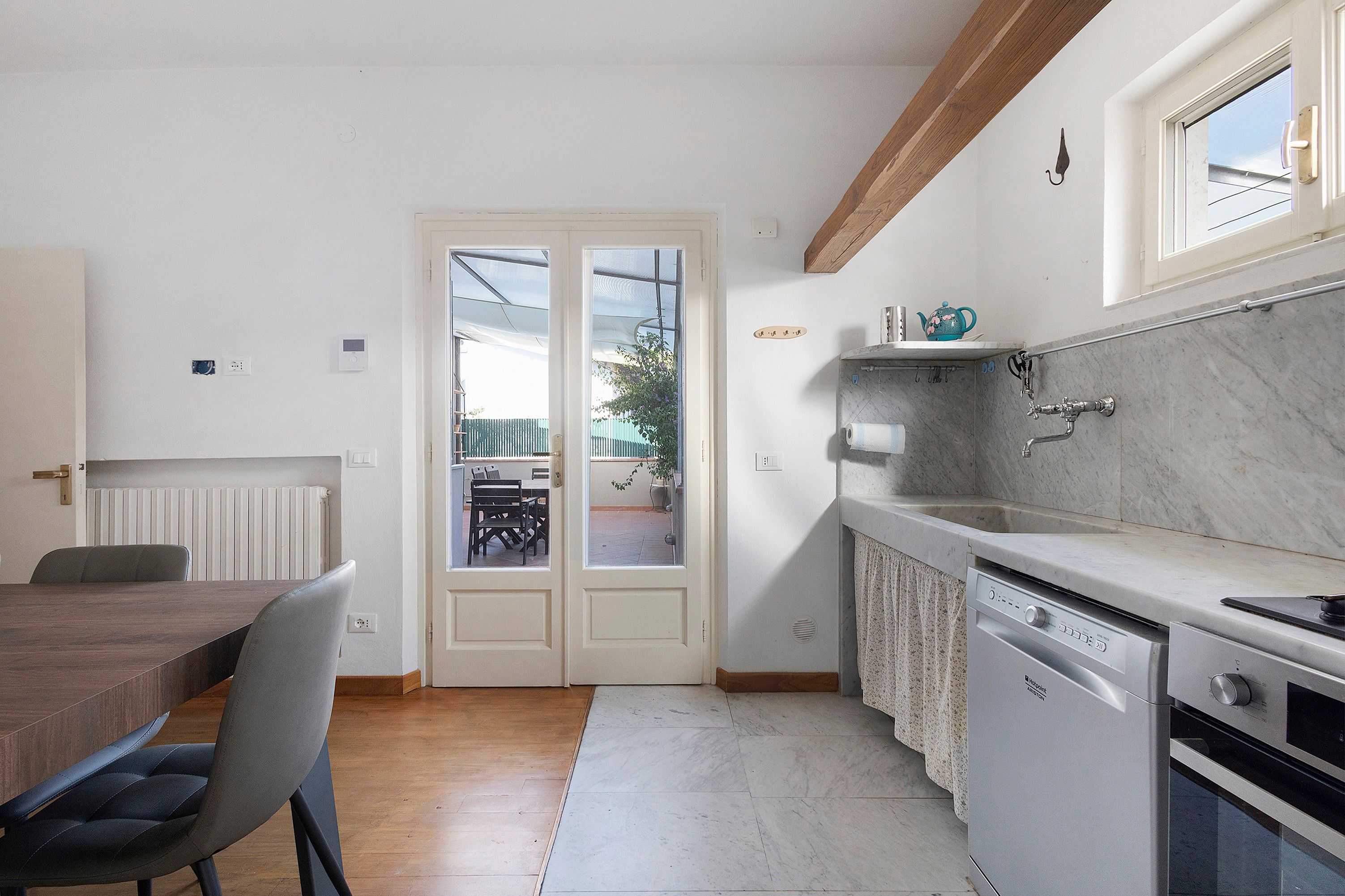 Une cuisine compacte comprenant un coin repas, un radiateur, un lave-vaisselle et une fenêtre donnant sur un balcon.