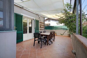 Un patio con una mesa y sillas, un toldo blanco y una cerca verde.