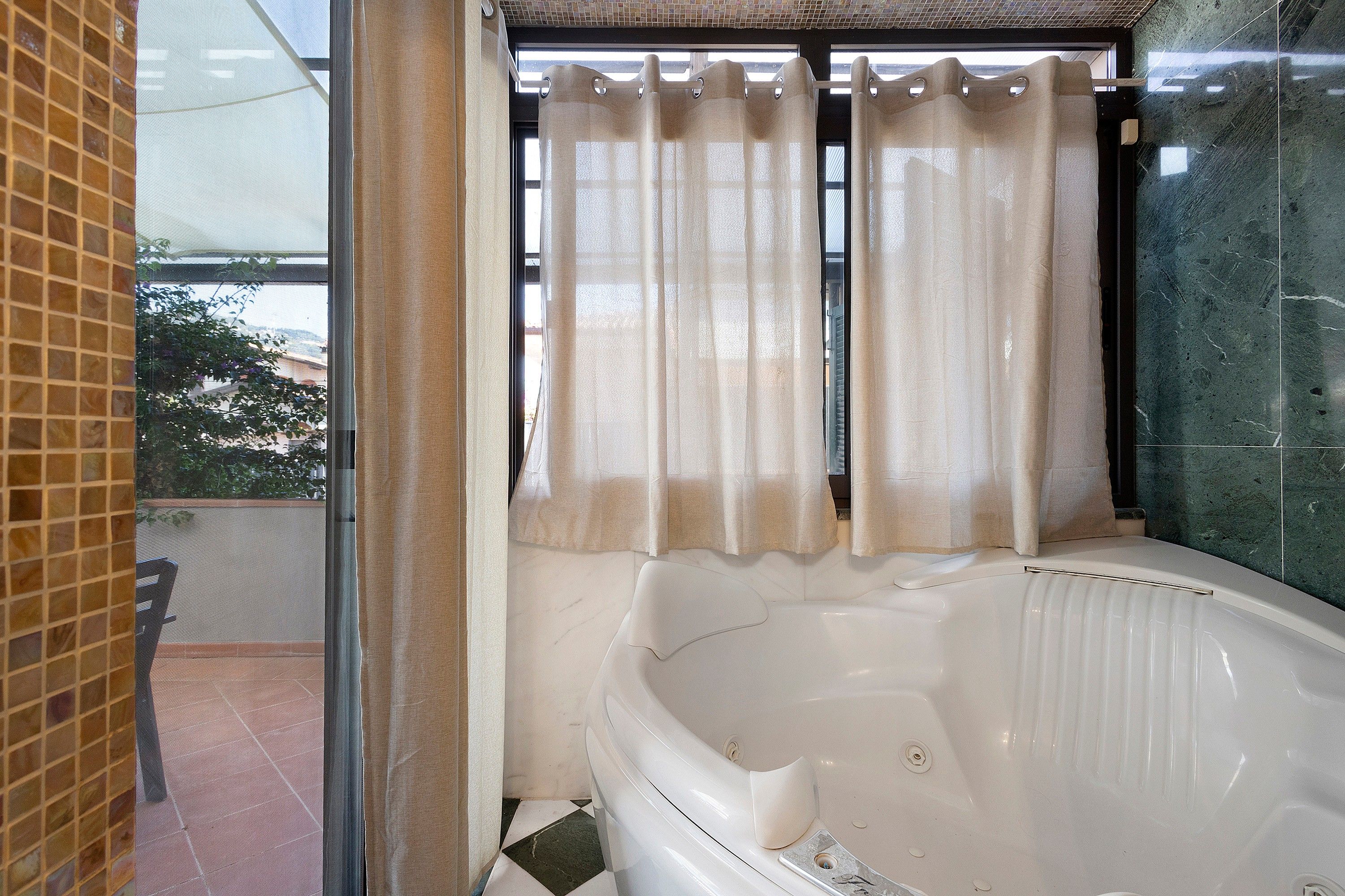 Ein Badezimmer mit einer Badewanne, einem Fenster mit Vorhängen und einem gefliesten Boden.