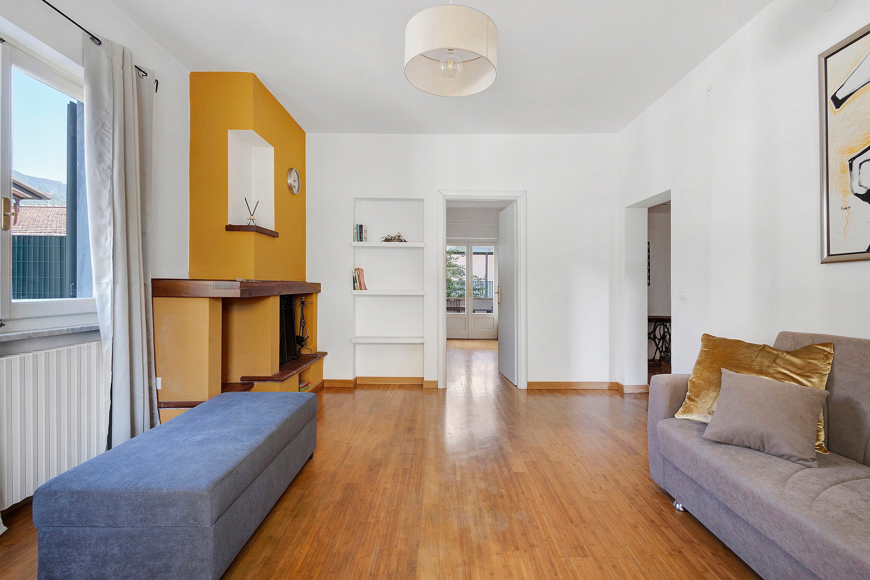 Una sala de estar con un sofá, una otomana y un comedor con una mesa y sillas. Hay un pasillo que conduce a otra habitación.