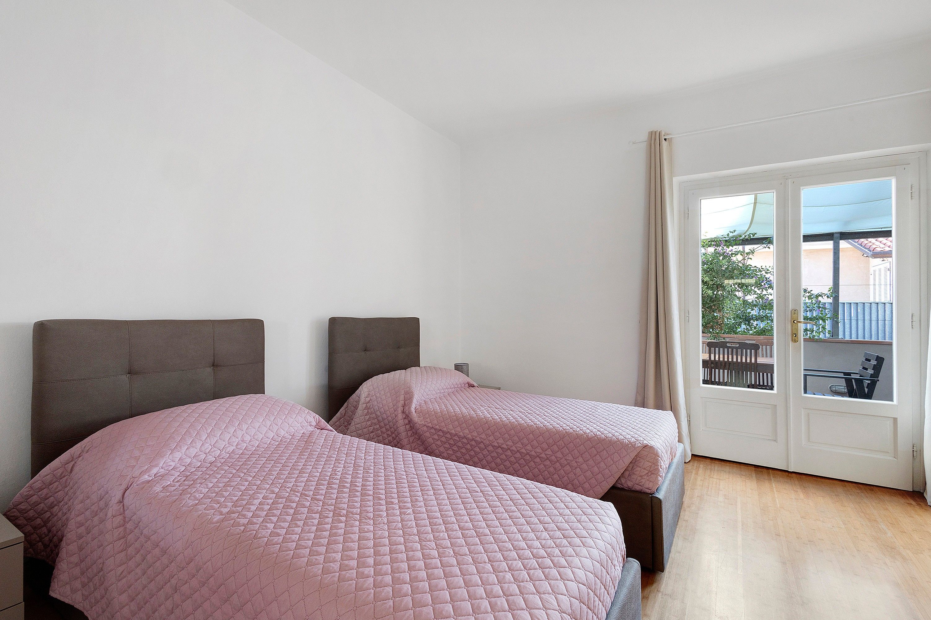 Una habitación con dos camas, una puerta que da al exterior y vistas a un balcón con plantas.