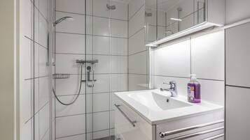 Ein modernes Badezimmer mit einer Duschkabine aus Glas, einem weißen Waschbecken und einem Spiegel sowie einer Seifenflasche.
