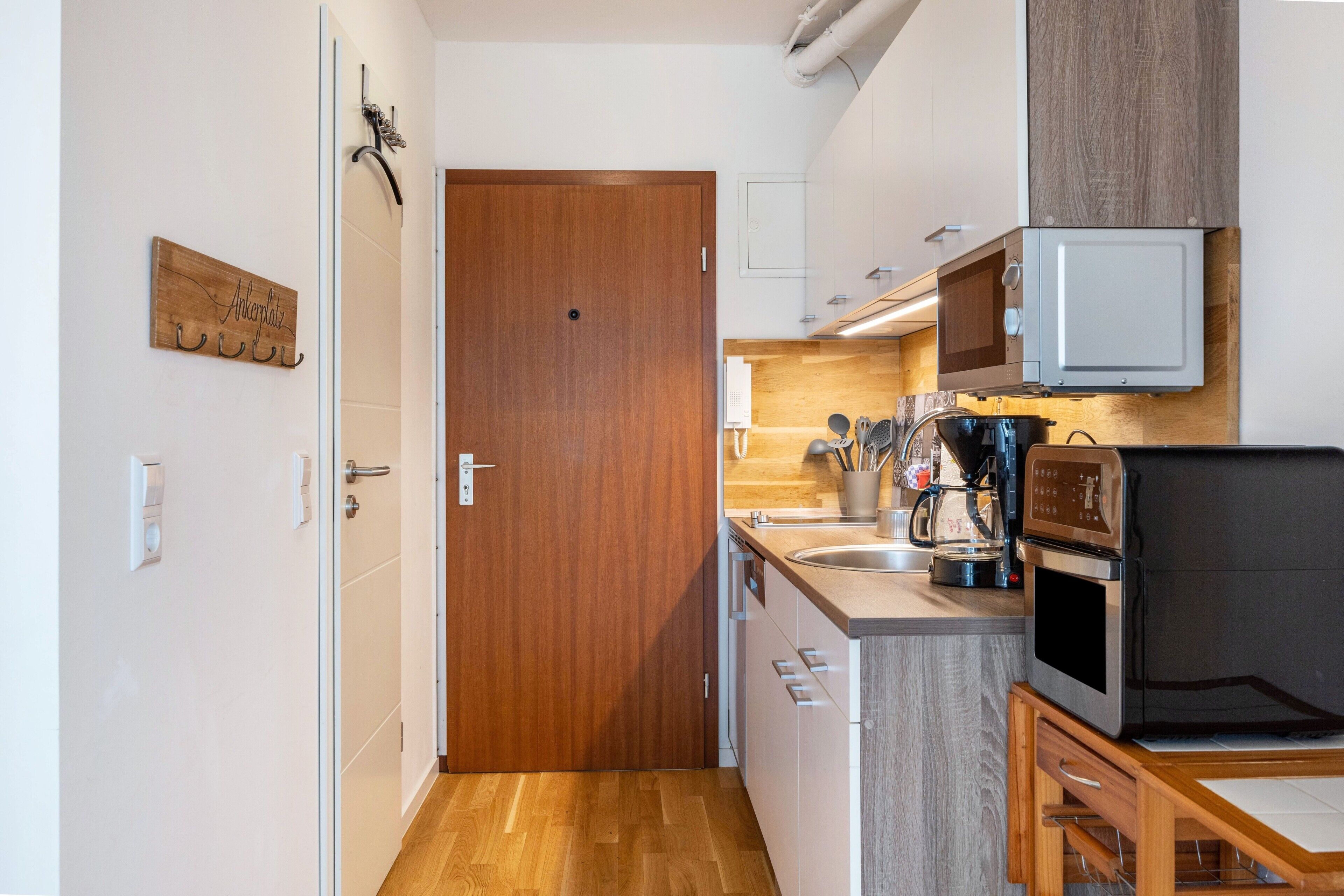 Cocina compacta con puerta de madera, microondas, cafetera y una pequeña mesa de comedor.