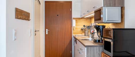 A compact kitchen with a wooden door, a microwave, a coffee maker, and a small dining table.