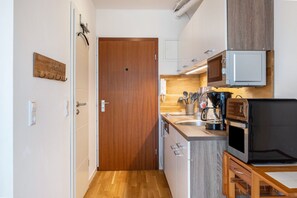 A compact kitchen with a wooden door, a microwave, a coffee maker, and a small dining table. - AnkerplatzSteinhuderMeer – Modern 2-Room Apartment with Balcony and Lake View (Wunstorf)