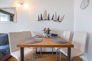 A dining area with a wooden table, four chairs, and a wall-mounted clock. - AnkerplatzSteinhuderMeer – Modern 2-Room Apartment with Balcony and Lake View (Wunstorf)
