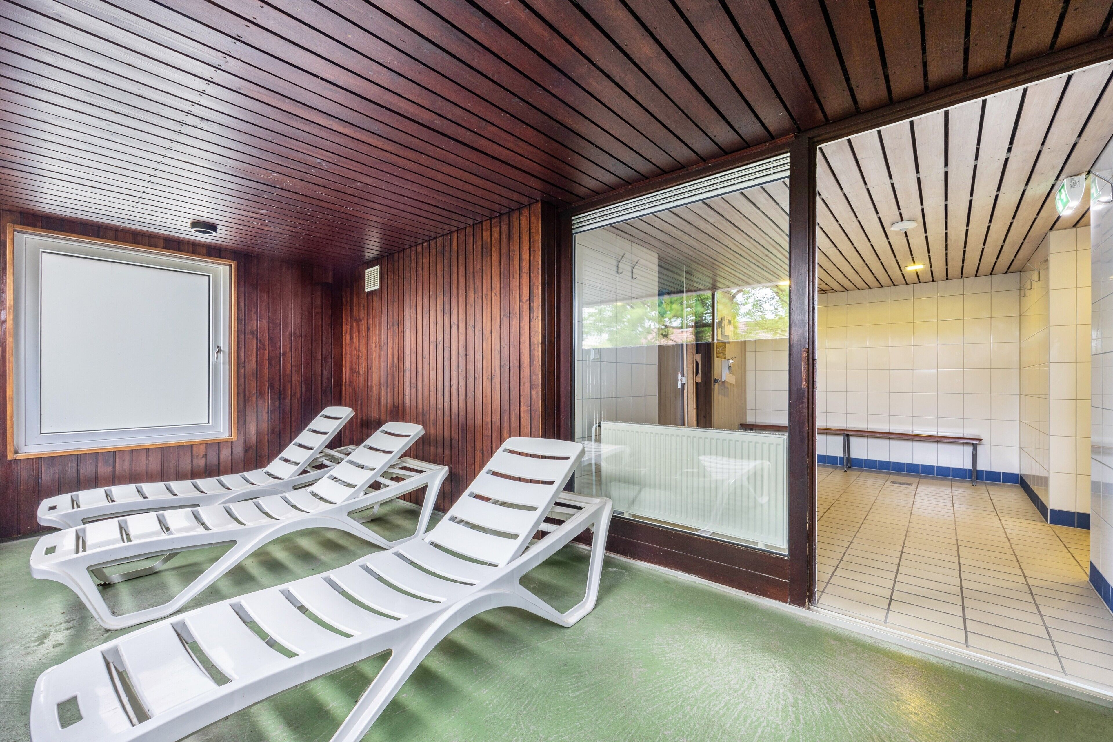 A spa area with wooden paneling, a glass door leading to a tiled room, and several white lounge chairs.