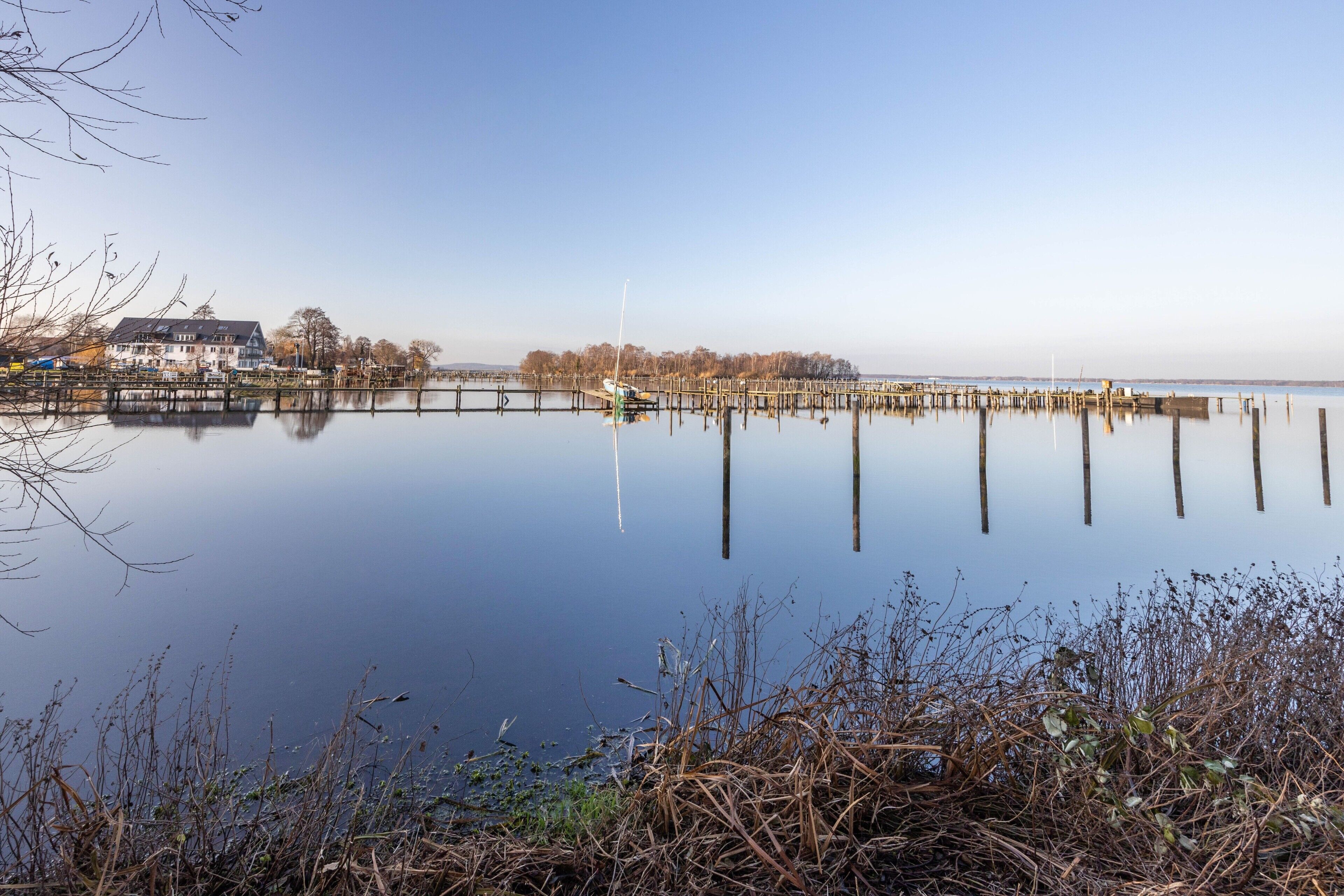 Un lac paisible avec une jetée qui s’avance sur l’eau, entouré d’arbres et bordé d’un bâtiment doté d’un toit en pente.