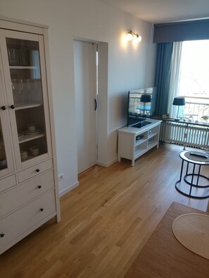 Ein modernes Wohnzimmer mit Holzboden, einer Vitrine, einem Fernsehschrank, einem kleinen Tisch und einem Fenster mit Vorhängen.