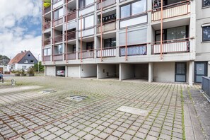 A multi-story residential building with balconies, a paved courtyard, and a car parked in front. - AnkerplatzSteinhuderMeer – Modern 2-Room Apartment with Balcony and Lake View (Wunstorf)