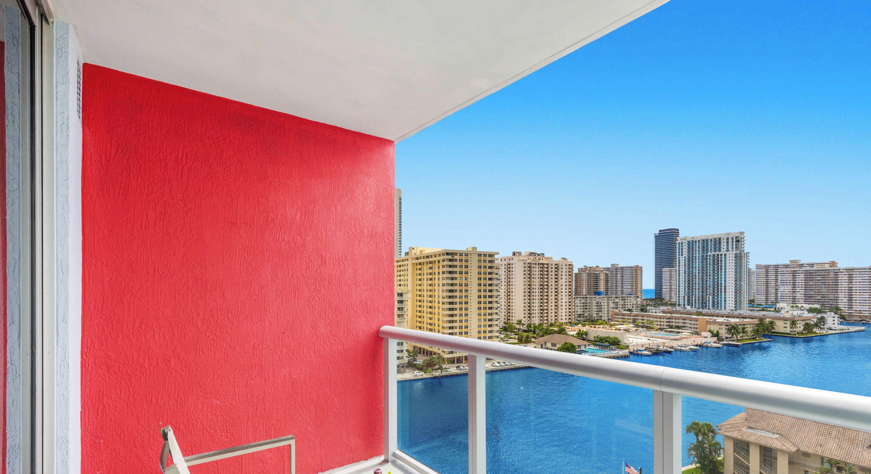 Ein Balkon mit roter Wand, Blick auf einen Yachthafen und eine Stadtlandschaft im Hintergrund.