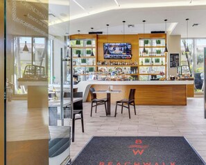 Un espace bar moderne avec un comptoir en bois, de nombreux types de sièges et un grand écran diffusant un événement sportif.