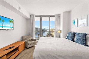 Quarto de hotel com cama, TV, escrivaninha, cadeira e vista para a cidade e para a água.