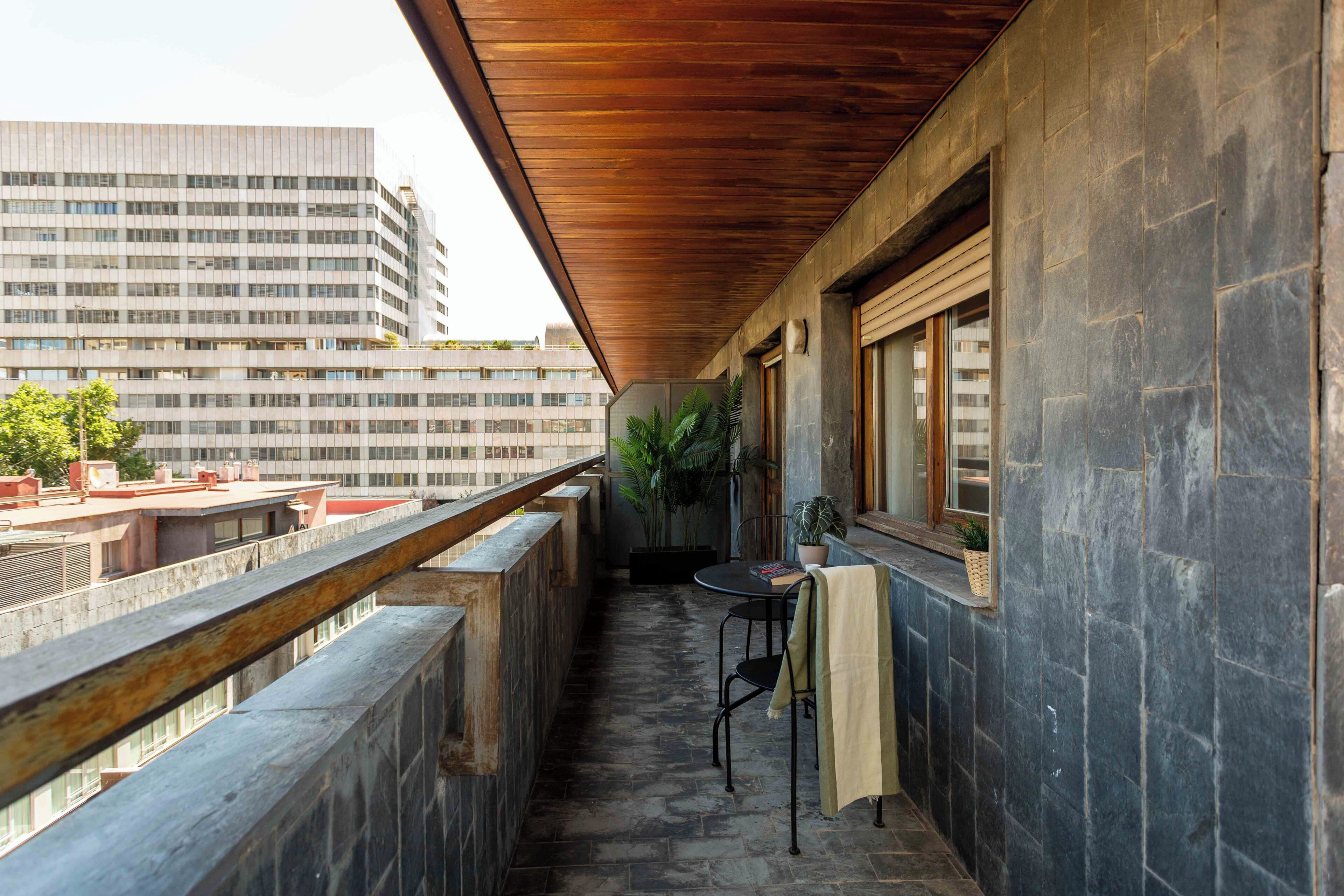 Un balcon doté d’un sol en pierre, d’un plafond en bois et offrant une vue sur un immeuble de grande hauteur.