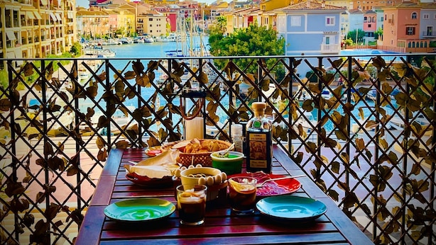 Un balcon avec une table dressée pour le dîner, donnant sur une marina où l’on peut admirer des bateaux et des bâtiments.