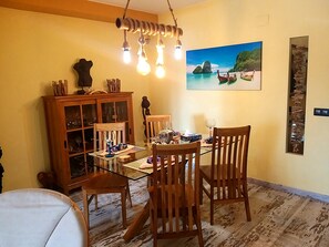 Een eethoek met een glazen tafel, houten stoelen, een kast met glazen deuren en een schilderij van een kustlandschap.