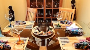 Une table ronde en verre, ornée d’un objet décoratif au centre, entourée de chaises et d’un buffet en bois doté de portes en verre.