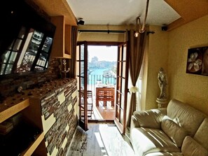 Een kamer met een stenen muur, een televisie, een standbeeld en uitzicht op een stadsbeeld door een open deur.