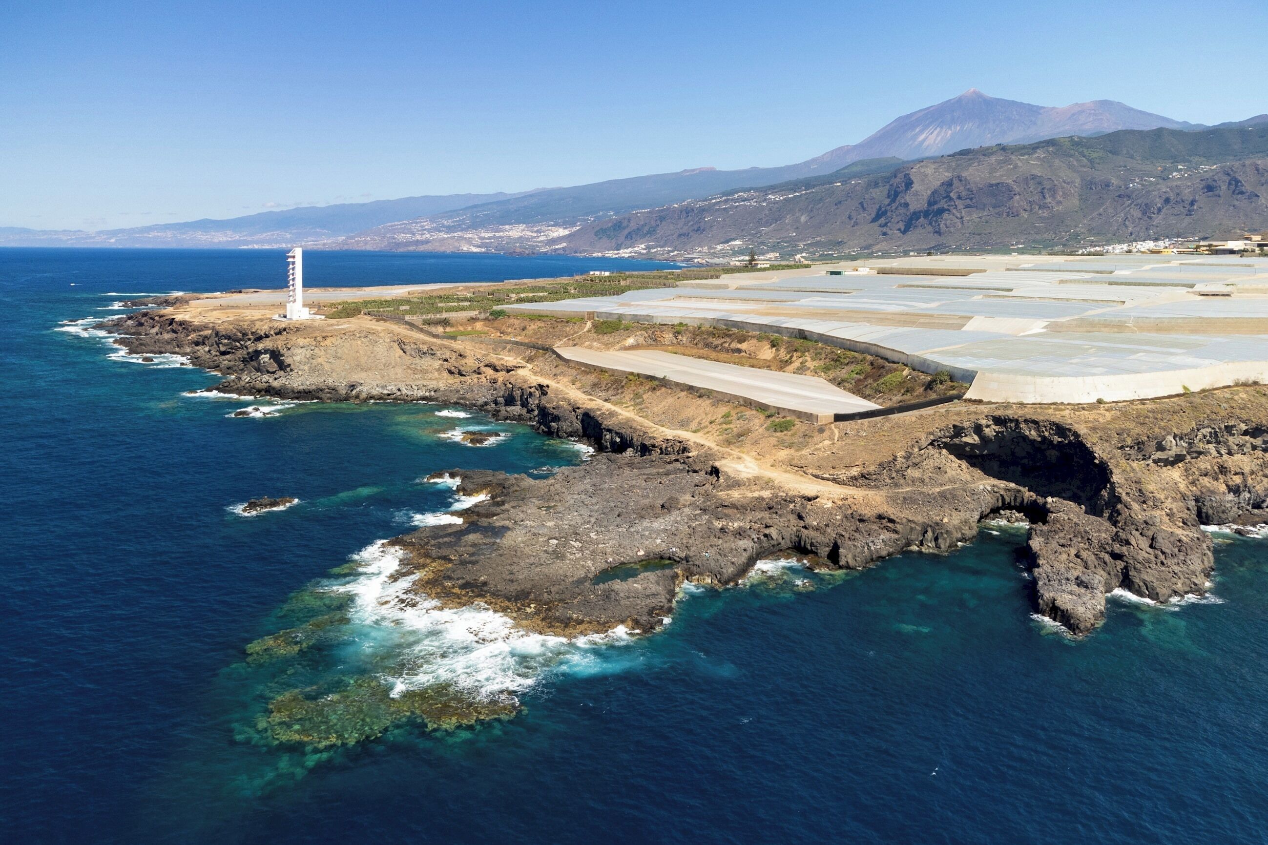 A coastal landscape with a lighthouse, rocky terrain, and a mountainous backdrop.