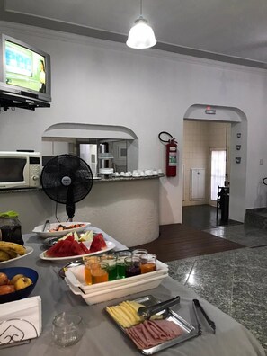 A buffet setup with various food items, a microwave, a fan, and a fire extinguisher. - Hotel Bela Vista Nova Odessa (Nova Odessa)
