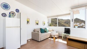 Ein Wohnzimmer mit einer Couch, einem kleinen Tisch, einer TV-Bank und einem Kühlschrank.