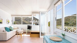 Ein modernes Wohnzimmer mit einer Couch, einem kleinen Tisch, einem Fernseher und einem Balkon mit Blick auf die Berge.