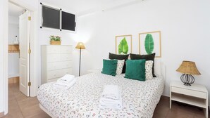 Ein Schlafzimmer mit einem Bett, einem Schminktisch, einem Nachttisch, einer Lampe und zwei gerahmten Blättern an der Wand.