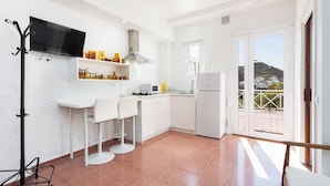 A modern kitchen with white cabinets, a flat-screen TV, and a view of a hillside through the sliding glass doors. - Home2Book Papaya Loft & Pool View (Santa Cruz de Tenerife)