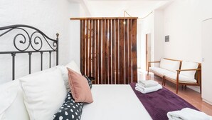 A bedroom with a bed, pillows, a wooden partition, a chair, and a bathroom visible in the background. - Home2Book Papaya Loft & Pool View (Santa Cruz de Tenerife)