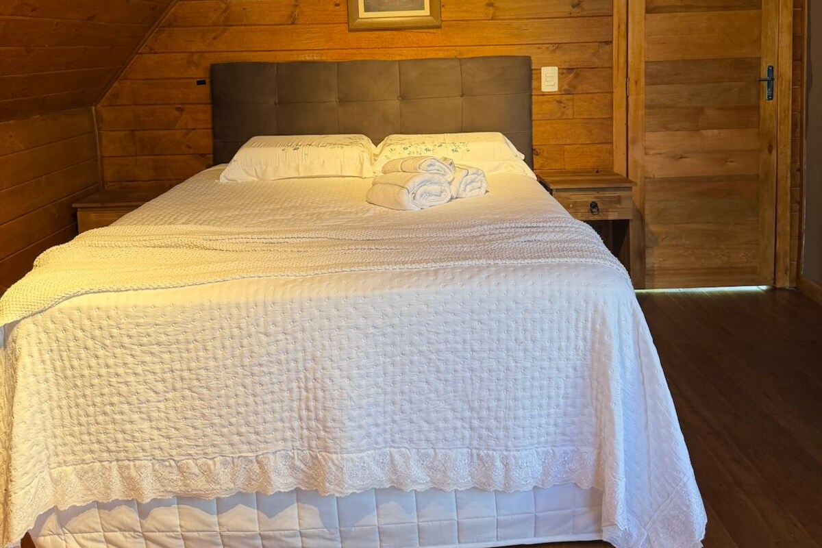 A bedroom with a wooden ceiling, a bed with white bedding, a nightstand, and a door.