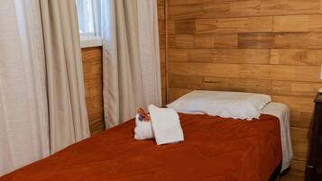 Quarto com parede de madeira, cama com colcha vermelha, almofadas brancas e janela com cortinas.