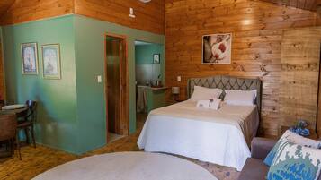 A wooden cabin bedroom with a bed, a chair, a table, and a door leading to a bathroom.