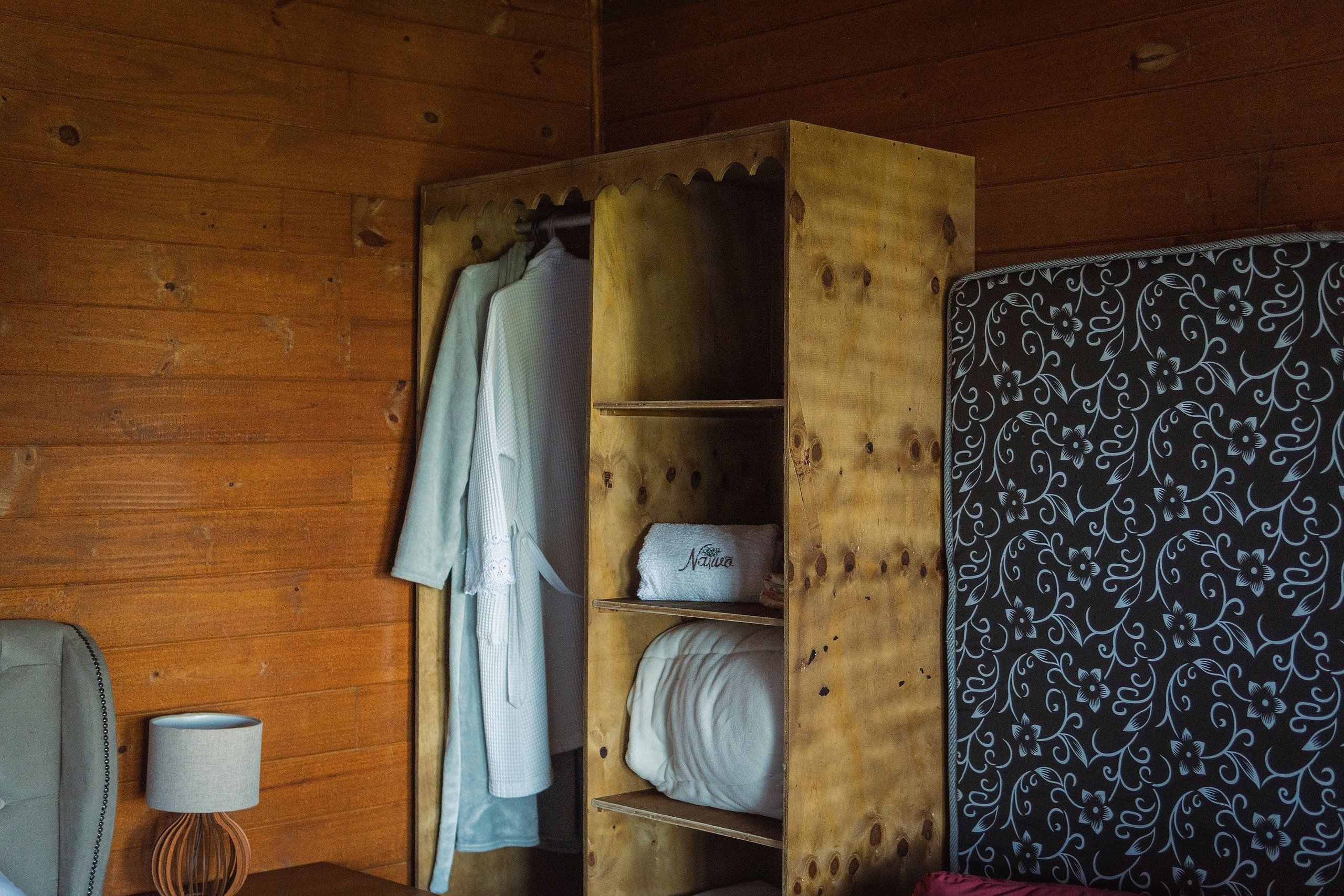 A wooden room with a bed, a nightstand with a lamp, and a wardrobe with shelves.