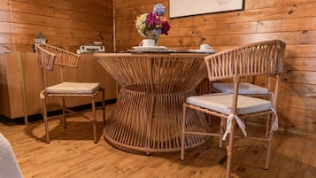 Ein Zimmer mit Holzvertäfelung, einem runden Korbstuhl, zwei Korbstühlen, einer kleinen weißen Tischlampe und einer Vase mit Blumen.