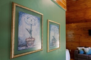 Dois quadros florais emoldurados numa parede verde, teto de madeira e um sofá com almofadas.
